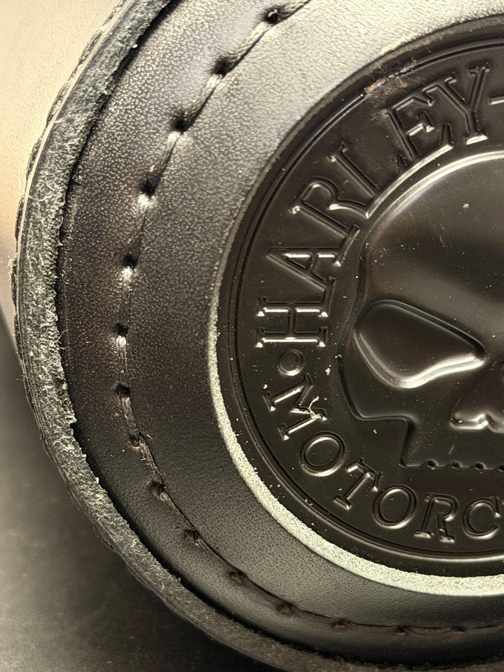 Close-up of a black leather motorcycle accessory with visible stitching and an embossed Harley-Davidson logo and skull on the side.